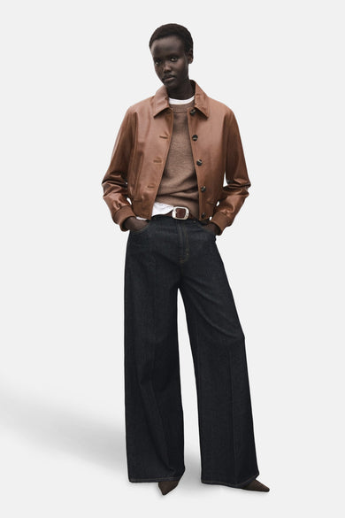 Pull marron avec col rond de MANGO, porté sous une veste en cuir et des jeans larges avec une ceinture marron.