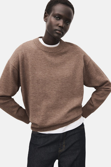 Pull marron avec col rond de MANGO, porté sur une chemise blanche et associé à un jean foncé.
