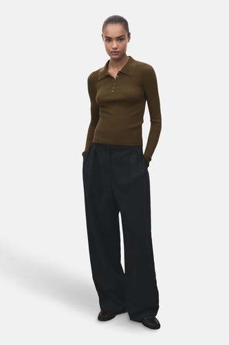 Gilet kaki avec col rond de MANGO, porté avec un pantalon noir à larges plis.