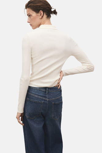 Gilet rond en beige de MANGO, avec des manches longues et un tissu côtelé fin, porté avec des jeans bleus foncés.