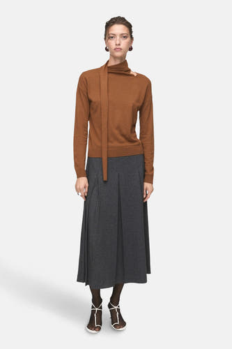 Pull marron avec col rond de MANGO, avec des manches longues et porté avec une jupe grise.