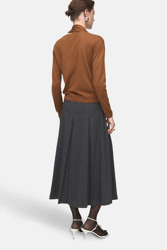 Pull marron avec col rond de MANGO, vu de derrière, associé à une jupe grise et des baskets blanches.