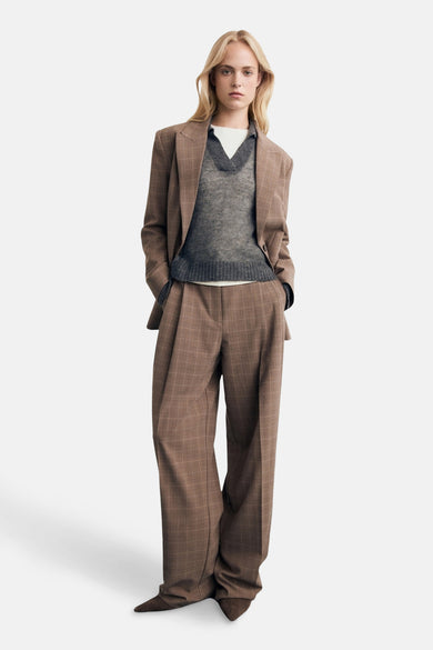 Pull à col V gris de MANGO, porté sur une chemise blanche et associé à un manteau kaki rayé.