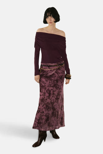 Veste Bordeaux avec col rond de MANGO, portée off-shoulder avec une longue jupe à motif floral violet et des bottes noires.