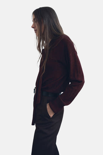 Veste Bordeaux avec col rond de MANGO, à longues manches et détail de cordon, associée à un pantalon foncé et une ceinture.