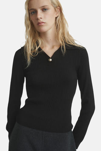 Pull noir avec col rond de MANGO, vu de derrière, associé à un pantalon gris foncé large et des mocassins bruns.