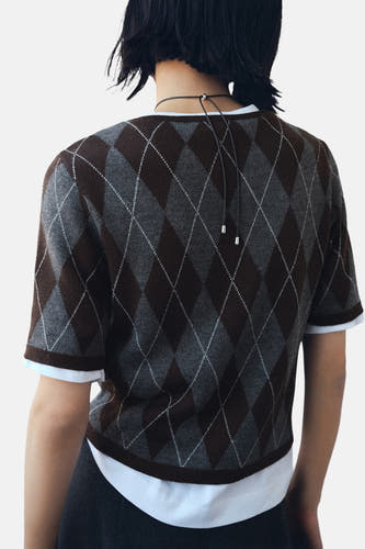 Sweat-shirt multicolore à col rond de MANGO, avec un motif carreaux d'argyle et des manches courtes, porté sur un T-shirt blanc.