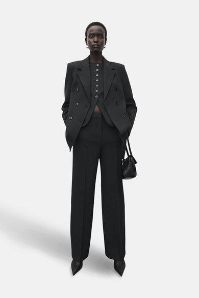 Pantalon gris de costume MANGO, combiné avec un blazer coordonné et une poche main noire.