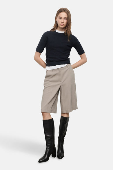 Blauwe trui met ronde hals van MANGO, gedragen met een wit T-shirt, beige shorts en zwarte leren laarzen.
