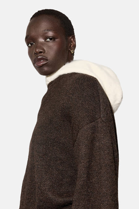 Pull marron avec col rond de MANGO, combiné à un capuchon blanc, associé à une pantalon blanc.