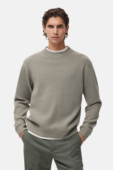 Pull-over gris à col rond de MANGO, vu de derrière, avec une subtile texture et un pantalon vert.