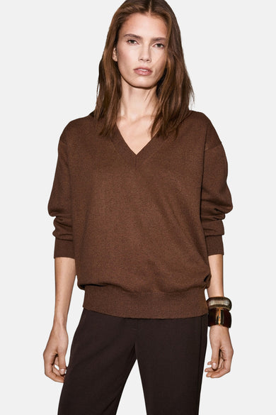 Pull marron avec col V de MANGO, vu de derrière, avec un pantalon coordonné et une bague d'or.