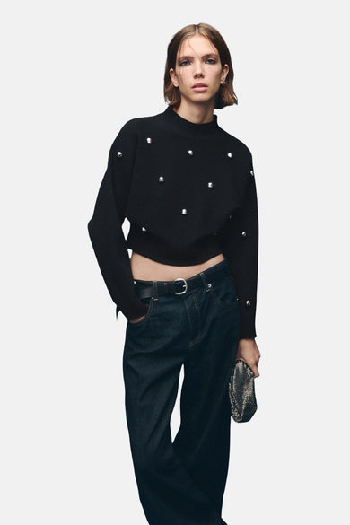 Pull-over noir à col rond de MANGO, vu de derrière, avec des manches longues et des poignets à boutons, associé à des jeans foncés.