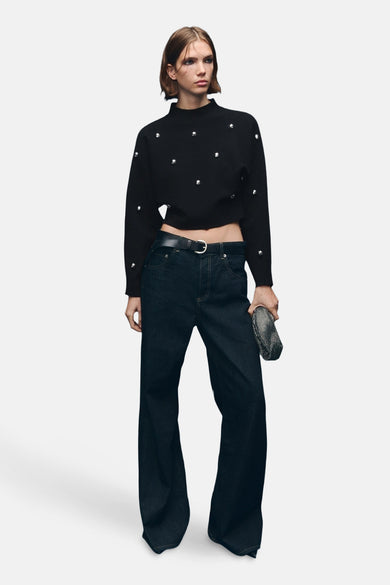 Zwarte trui met ronde hals van MANGO, versierd met zilverkleurige studs, gecombineerd met donkerblauwe wijde jeans en een zilveren clutch.