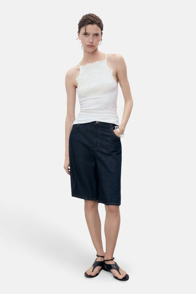 T-shirt blanc avec des bandes de spaghetti de MANGO, avec un détail crocheté et associé à des shorts en denim Bermuda et des sandales.