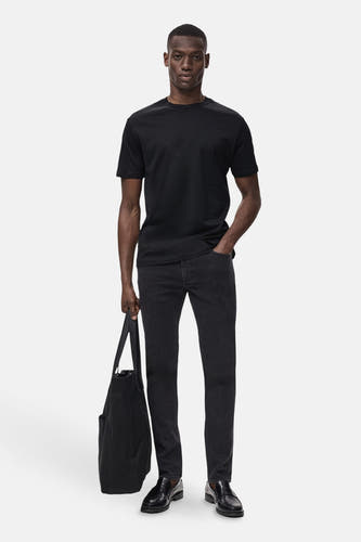 Jean slim fit couleur gris foncé de MANGO, associé à un T-shirt noir, des loafers en cuir et une sacoche noire.