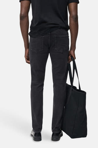 Jean slim gris foncé de MANGO, avec des poches arrière et porté avec un T-shirt noir et une sacoche.