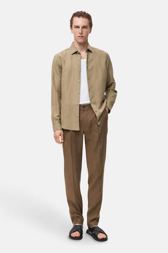 Chemise kaki à manches longues de MANGO, portée avec un t-shirt blanc et des pantalons marron avec des sandales en cuir.
