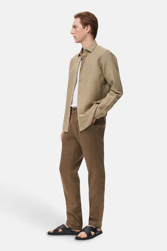 Kaki overhemd met lange mouwen van MANGO, gedragen over een wit t-shirt, met bruine broek en zwarte sandalen.