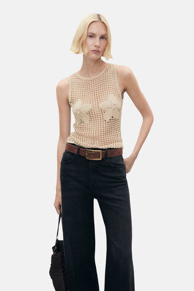 T-shirt beige MANGO avec des détails floraux, associé à une ceinture marron et des jeans noirs.