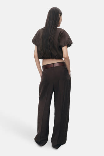 Blouse brune à manches courtes de MANGO, vue de derrière, avec un pantalon foncé et une ceinture.