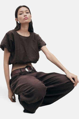 Blouse brune à manches courtes de MANGO, portée avec un pantalon brune et une cece avec boucle en argent.