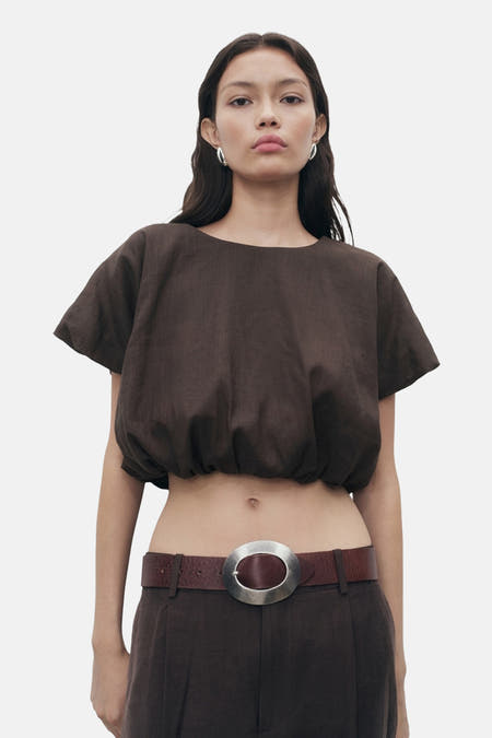 Blouse brune à manches courtes de MANGO, avec un élastique et portée avec une ceinture brune à boucle argentée.