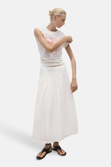 T-shirt blanc à manches courtes de MANGO, avec un imprimé rose "la fraise" et porté avec une jupe blanche et des sandales.