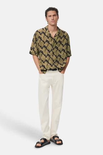 Chemise multicolore à manches courtes de MANGO, avec un motif géométrique, portée avec un jean blanc et des sandales.