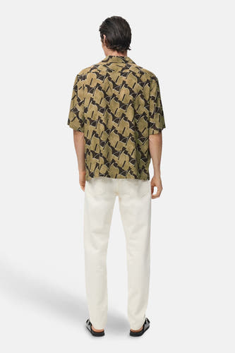 Chemise multicolore à manches courtes de MANGO, avec un motif abstrait et portée avec un pantalon blanc.