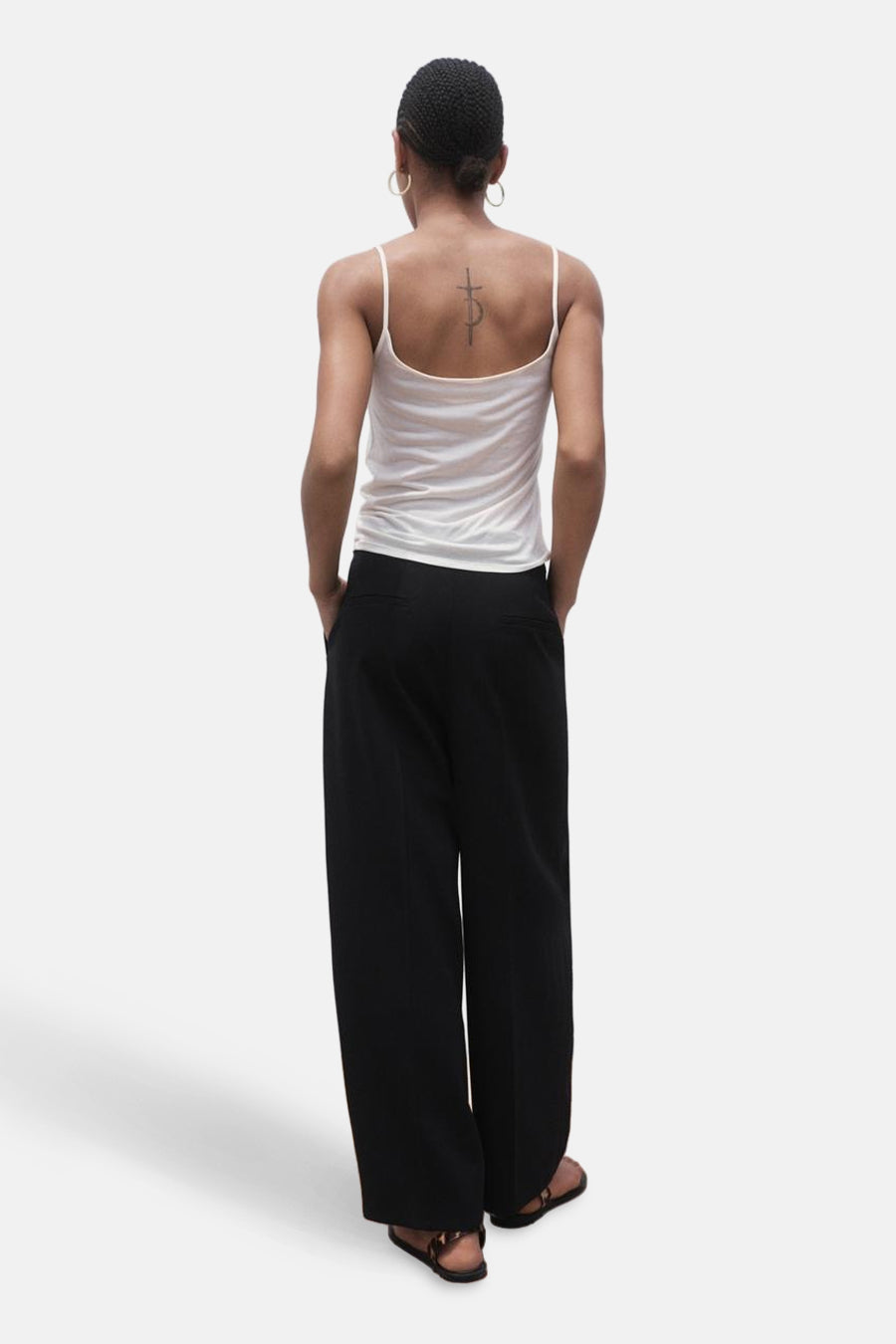 Pantalon de costume noir MANGO, vu de l'arrière, avec des jambes larges et une chemise coordonnée.