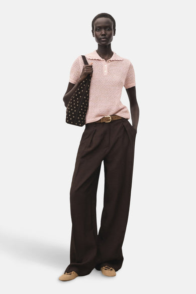 Polo rose à manches courtes de MANGO, avec une texture ouverte et porté avec un pantalon marron et une sacoche.