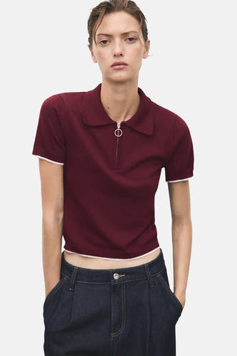 Veste Bordeaux avec col rond de MANGO, manches courtes et fermeture à glissière devant, associée à des jeans foncés.