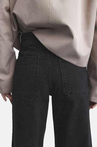 Jean large noir de MANGO, avec des poches brodées sur l'arrière, associé à une veste taupe.