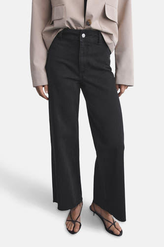 Jean boyfriend large de MANGO, associé à une veste beige et des sandales à brides.