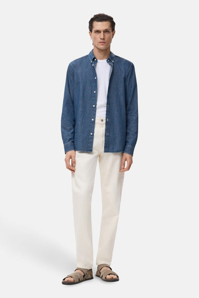 Chemise en denim à manches longues de MANGO, portée sur un T-shirt blanc et associée à une pantalon crème et des sandales brunes.