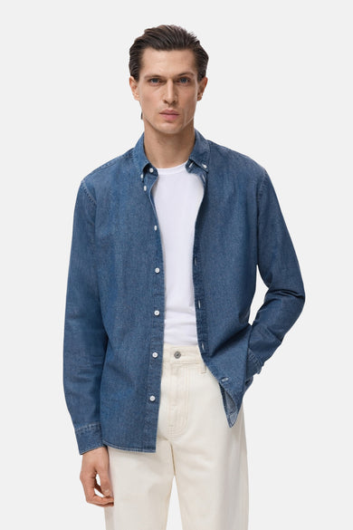 Chemise en denim à manches longues de MANGO, portée sur un T-shirt blanc et une pantalon beige.