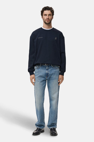 Pull-over bleu de MANGO, avec petit logo sur la poitrine, associé à des jeans et des chaussures en cuir.