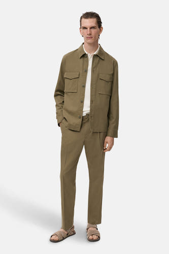 Pantalon khaki de MANGO, porté avec un t-shirt beige et des sandales, debout contre un fond blanc.