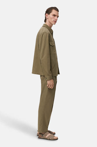 Pantalon kaki de MANGO, vu de en profil, associé à une chemise kaki et des sandales en cuir.