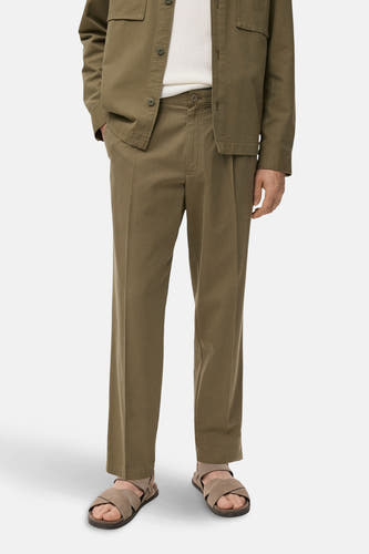 Pantalon khaki de MANGO, avec plis et jambes droites, associé à des sandales et une chemise verte.