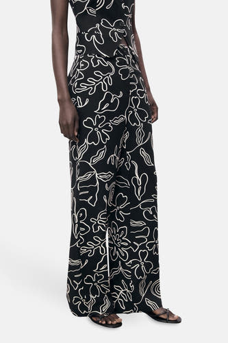 Pantalon noir de MANGO avec un motif floral blanc, des jambes largement évasées et des sandales.