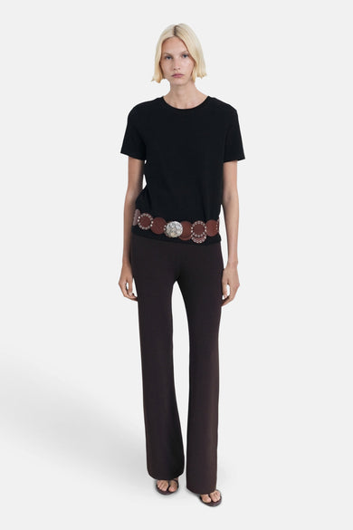 T-shirt noir à manches courtes de MANGO, porté avec une ceinture marron et des disques décoratifs et un pantalon marron.