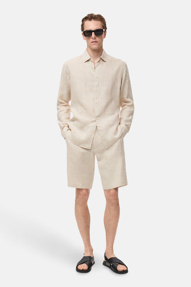 Chemise beige à manches longues de MANGO, portée avec un short coordonné et des sandales noires.