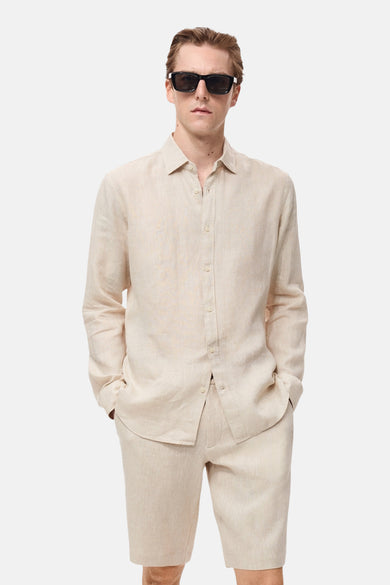 Chemise de lin beige à longues manches de MANGO, portée avec des shorts et un chapeau.