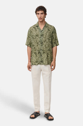 Chemise verte à manches courtes de MANGO, avec un motif triangulaire abstrait, associée à des pantalons crème et des sandales.