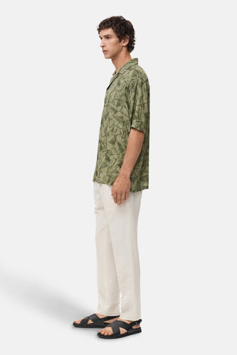 Chemise verte à manches courtes de MANGO, avec un motif géométrique, associée à des pantalons en lin légers et des sandales.