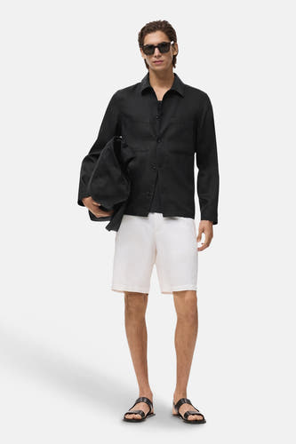 Manteau court noir de MANGO, porté avec des short blancs et des sandales.