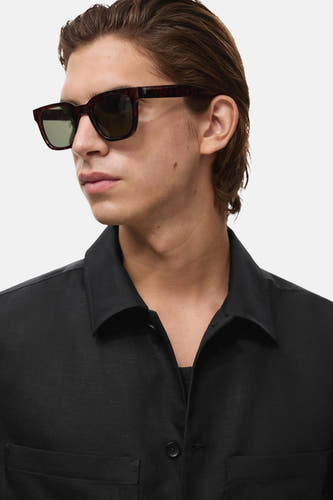 Manteau court noir de MANGO, porté avec un t-shirt noir, doté d'une poche poitrine et d'un soleil.