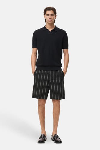 Short noir de MANGO, avec des rayures de craie et des poches, associé à un polo noir et des loafers en cuir.